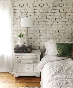 a white bed sitting next to a window in a room with wooden floors and brick walls