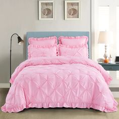 a bed with pink comforter and pillows in a room next to a lamp on a table