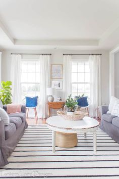 a living room with two couches and a table in front of the window on top of a striped rug