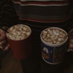 two cups of hot chocolate with marshmallows in them are being held by someone