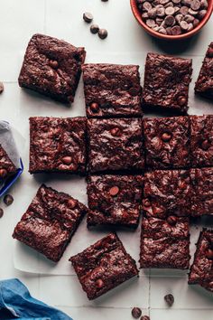 chocolate brownies cut into squares and placed next to a bowl of chocolate chips on a white surface