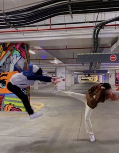 two people are doing tricks in an empty parking garage with graffiti on the wall behind them