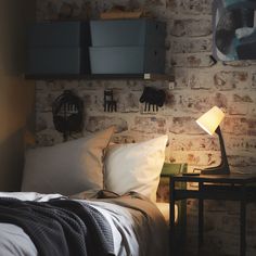 a bedroom with brick wall and white bedding, two night stands on either side