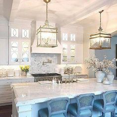 a large white kitchen with blue chairs and marble counter tops on the island in front of it