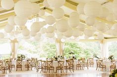 a room filled with tables and chairs covered in white paper lanterns hanging from the ceiling