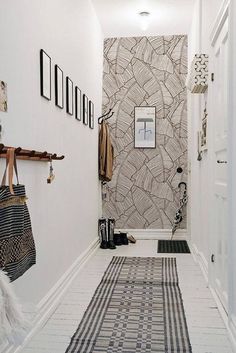 a hallway with white walls and black and white patterned rugs on the floor next to a coat rack