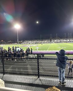 a group of people standing on top of a soccer field at night with the lights on