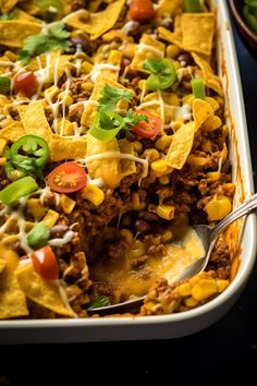 a casserole dish filled with taco meat, beans, cheese and tortilla chips