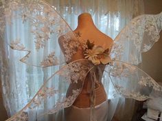 a mannequin with white lace and flowers on it's back, in front of a window