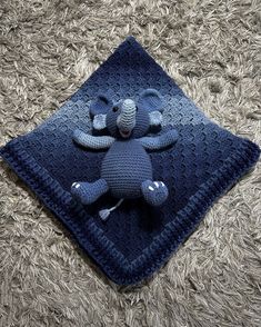 a blue crocheted stuffed animal laying on top of a square shaped blanket with an elephant