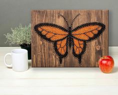 an orange and black butterfly is on a wooden plaque next to a white coffee cup