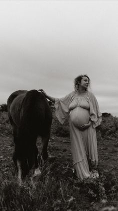 a pregnant woman standing next to a cow in a field with cloudy sky behind her