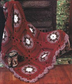 a red crocheted blanket sitting on top of a wooden floor next to a fire place