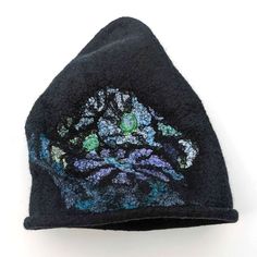 This Nunofelted Beanie Cap in Black Merino Wool is a stylish and practical accessory that is good for any occasion. Its playful design features a cheeky tip that angles to one side, adding a touch of whimsey to your look. The hat is wet felted from high-quality Merino wool roving, making it lightweight and easy to wear. The stained glass pattern on the beanie is inspired by the iconic floral motifs of Harry Clarke, giving it a unique and artistic appeal. Whether you are exploring the seaside or Handmade Black Felt Hat For Winter, Harry Clarke, Felted Hat, Stained Glass Pattern, Wool Roving, Wet Felt, Elf Hat, Small Towel, Glass Pattern