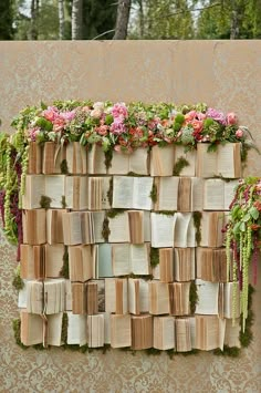 an arrangement of books are arranged on a wall made out of flowers and mosss