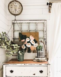 a white dresser topped with flowers next to a clock on top of a wooden table