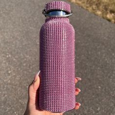 a hand holding a purple bottle on the side of a road with grass in the background