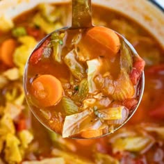 a spoon full of soup with carrots and other vegetables in it, being held up by a ladle