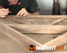 a man sitting at a table working on some wood pieces with a pencil in his hand