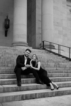 a man and woman sitting on the steps in front of a building with stairs leading up to them