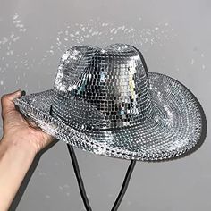 a person's hand holding up a shiny silver hat that is falling into the air