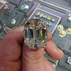 someone is holding an emerald colored diamond in their hand, surrounded by other jewelry pieces