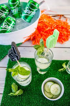 two glasses filled with cucumber and mint water on top of green grass next to carrots