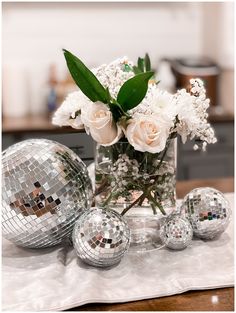 a vase filled with white flowers sitting on top of a table next to disco balls