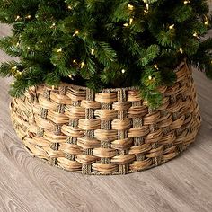 a christmas tree in a woven basket with lights on the top and below it, sitting on a wooden floor