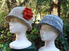 two crocheted hats with red flowers on them sitting on top of white mannequin heads