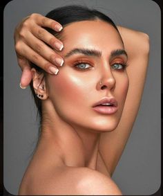 a woman with her hands on her head and one arm behind her head, wearing gold makeup