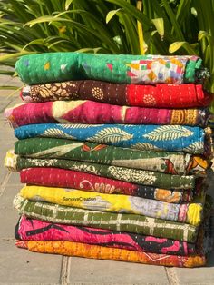 a stack of colorful cloths sitting on top of a stone floor next to green plants