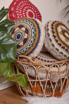 three decorative pillows sitting in a basket next to a potted plant