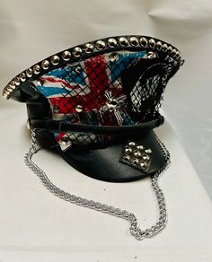 This is a black leatherette captain hat. Well made to a high standard. It has plenty of eye catching detail including metal studs, safety pins and Union Jack  , please refer to photos . It also has a metal chain, This is a size 59 cm which fits most size heads. No two hats are created the same. Individual and unique  Thank you for looking Black Punk Brimmed Hats, Black Brimmed Punk Hat, Black Punk Top Hat For Alternative Fashion, Adjustable Brimmed Punk Style Costume Hats And Headpieces, Punk Brimmed Hat For Festival, Punk Brimmed Hat For Alternative Fashion, Punk Style Brimmed Top Hat For Parties, Black Adjustable Punk Mini Hat, Adjustable Black Punk Mini Hat