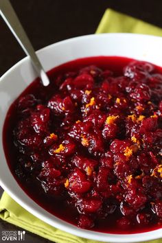 a white bowl filled with cranberry sauce on top of a yellow napkin next to a spoon