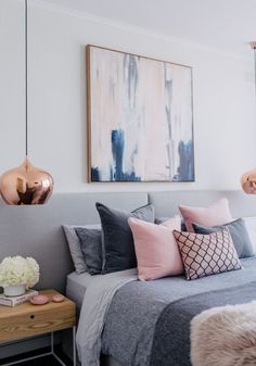 a bedroom with pink and grey pillows on the bed, two hanging lights above the bed