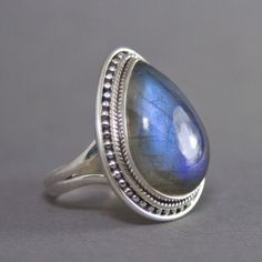 SKU: SS-007Material: 925 stamped sterling silverGemstone(s): Labradorite (N)Gemstone Dimensions: 15 X 22 X 5 mmRing Size: US 7.5Weight: 9.4 gramsThis breathtaking Labradorite cabochon ring is truly a beauty! Set in a classic bezel with a granulated border, the setting enhances the large Labradorite beautifully. The Labradorite not only has a strong blue fire that can be seen from every angle, it also has mica flakes, which add that extra shimmer to an already incredible stone! Teardrop Moonstone Ring In Sterling Silver, Silver Teardrop Moonstone Ring For Anniversary, Sterling Silver Teardrop Moonstone Ring, Sterling Silver Teardrop Gemstones For Anniversary, Silver Teardrop Moonstone Ring In Sterling Silver, Silver Teardrop Gemstones, Silver Teardrop Rings With Spiritual Style, Teardrop Sterling Silver Gemstone For Anniversary, Silver Pear-shaped Moonstone Ring