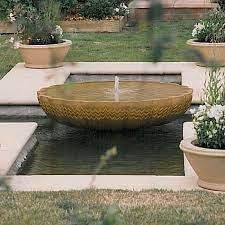 a water fountain surrounded by potted plants in a garden area with grass and flowers