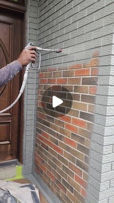 a man using a hose to spray paint on a brick wall in front of a door