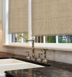 a kitchen sink under a window with roman shades