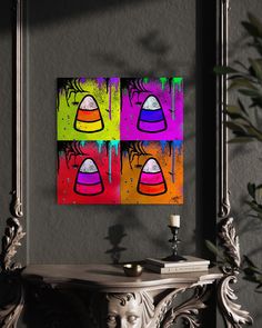 two colorful paintings are hanging on the wall next to a small table with a candle