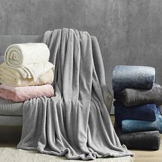 towels and blankets are stacked on a couch in front of a gray wall with a white rug