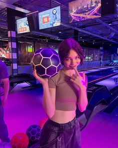 a woman holding a purple ball in her right hand while standing next to bowling lanes