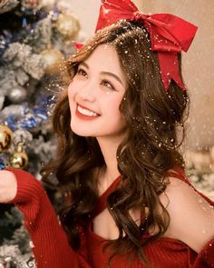 a beautiful young woman holding a christmas ornament in front of a christmas tree