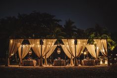 an outdoor wedding setup with draping and lights in the dark, surrounded by palm trees