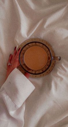 a woman's hand holding a cup of coffee on top of a white sheet