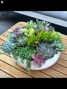 a white bowl filled with lots of succulents on top of a wooden table