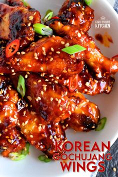 a white plate topped with chicken wings covered in sauce and sesame seeds, garnished with green onions