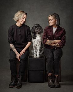 two women sitting next to each other with a dog in front of them on a black box