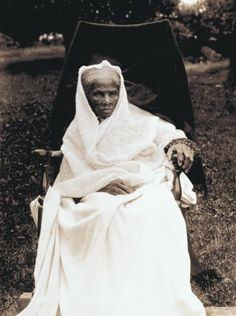 an old woman sitting in a chair with a shawl on her head and wearing a white dress